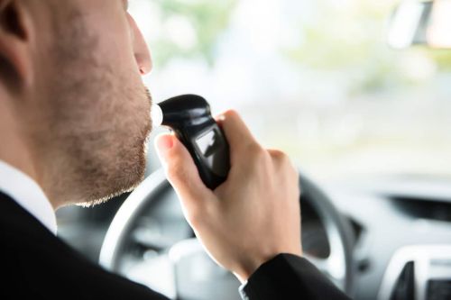 Close-up Of A Man Sitting Inside Car Taking Alcohol Test - ignition interlock device laws concept